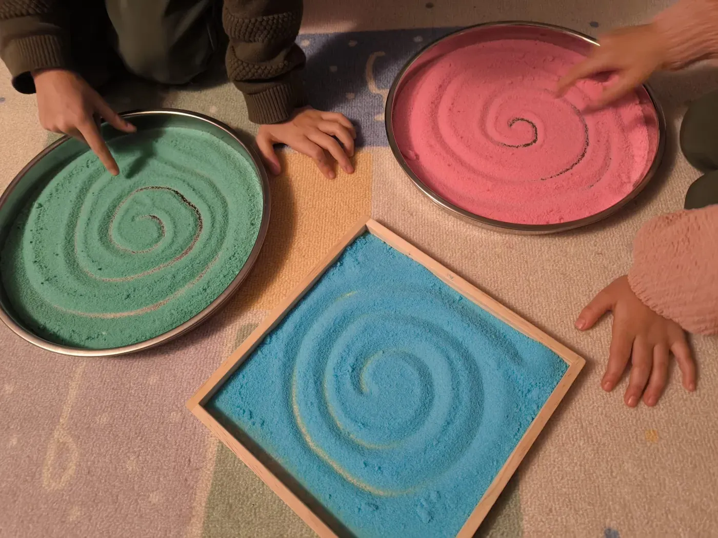 Kinderhände zeichnen Spiralen in farbigen Sand, Übung für Wahrnehmung und Feinmotorik
